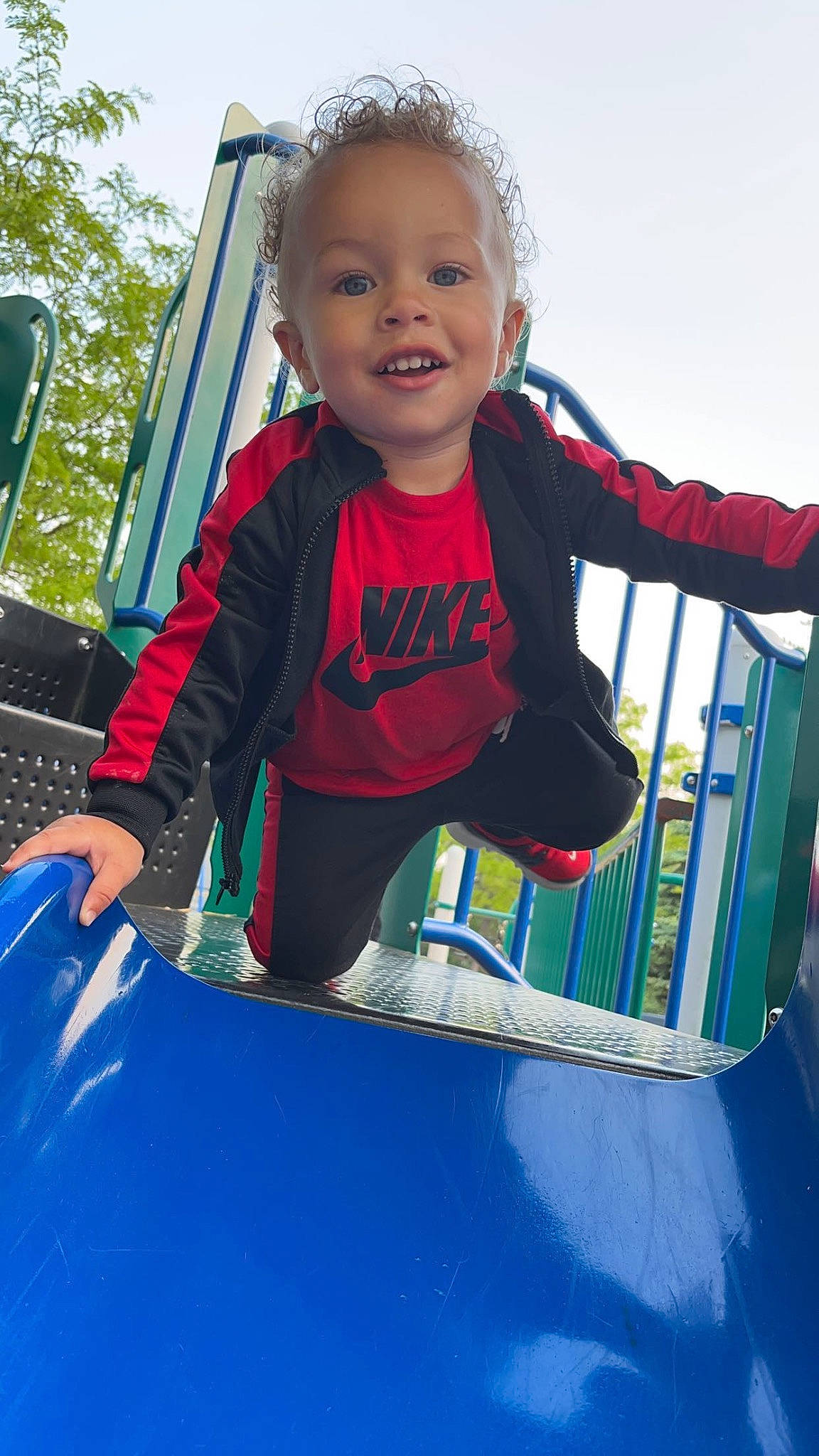 Kyden is registered to the contest to win money with this photo: baby, baby_toddler_clothing, blue, chute, city, electric_blue, fun, happy, hood, leisure, motor_vehicle, outdoor_play_equipment, person, playground, recreation, sky, smile, t_shirt, toddler, tree