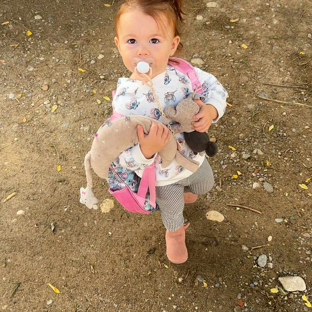 Heiana participe au concours pour gagner de l'argent avec cette photo : backpack, boots, casual_clothing, child, curious, daylight, dirt, gravel, long_sleeve, nature, outdoor, pacifier, patterned_pants, playful, plush_toy, small_person, standing, toddler, vehicle_tire, young_child