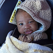 Cairo is registered to the contest to win money with this photo: baby, child, blanket, hoodie, car_seat, smile, face, cute, infant, warm_clothing, soft_texture, portrait, indoors, cozy, headwear, person, expression, seatbelt, warning_label, closeup