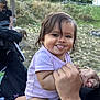 baby, child, tongue_out, smiling, holding_hands, outdoor, nature, grass, leaves, person, clothing, onesie, happy, cute, face, hair, skin, hand, playful, expression
