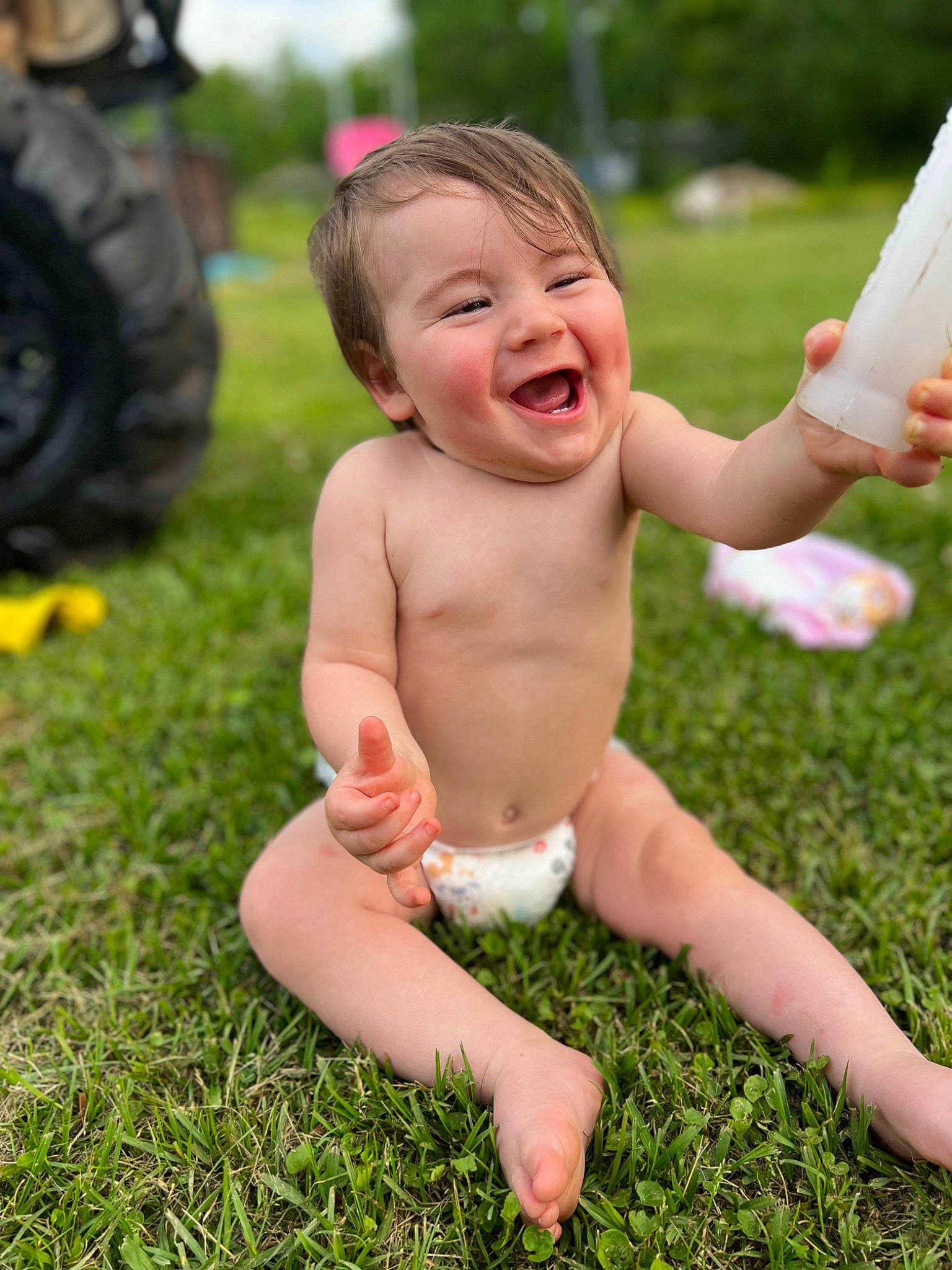Gunnar is registered to the contest to win money with this photo: automotive_tire, face, finger, fun, gesture, grass, hand, happy, head, human_body, leisure, people_in_nature, person, plant, skin, smile, thumb, tire, toddler, tractor