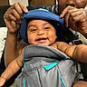 baby, child, smiling, blue_hat, baby_carrier, adult_hands, indoor, person, happy, closeup, face, infant, cute, joy, parent, bonding, skin, clothing, seat, love