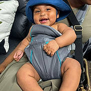Dinero is registered to the contest to win money with this photo: baby, blue_hat, baby_carrier, smiling, child, infant, person, couch, leather, pillow, adult, hand, clothing, seat, happy, indoor, closeup, cute, portrait, babywearing