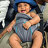 baby, blue_hat, baby_carrier, smiling, child, infant, person, couch, leather, pillow, adult, hand, clothing, seat, happy, indoor, closeup, cute, portrait, babywearing