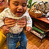 baby, child, smiling, jeans, pajamas, hands, person, indoor, wood_floor, basket, plant, books, furniture, couch, lamp, happy, holding, blue_socks, portrait, living_room