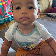 Théo a rejoint le concours — aidez-le/la à gagner de superbes lots ! toddler, child, sitting, indoor, face, curly_hair, shorts, tshirt, expressionless, carpet, couch, blanket, person, home, floor, hand, foot, young_child, casual_clothing, portrait
