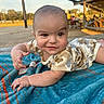 baby, blanket, blue_blanket, camouflage_clothing, child, crawling, eyes, face, hands, infant, lying_down, onesie, outdoors, park, pavilion, picnic, playground, portrait, smiling, sunlight