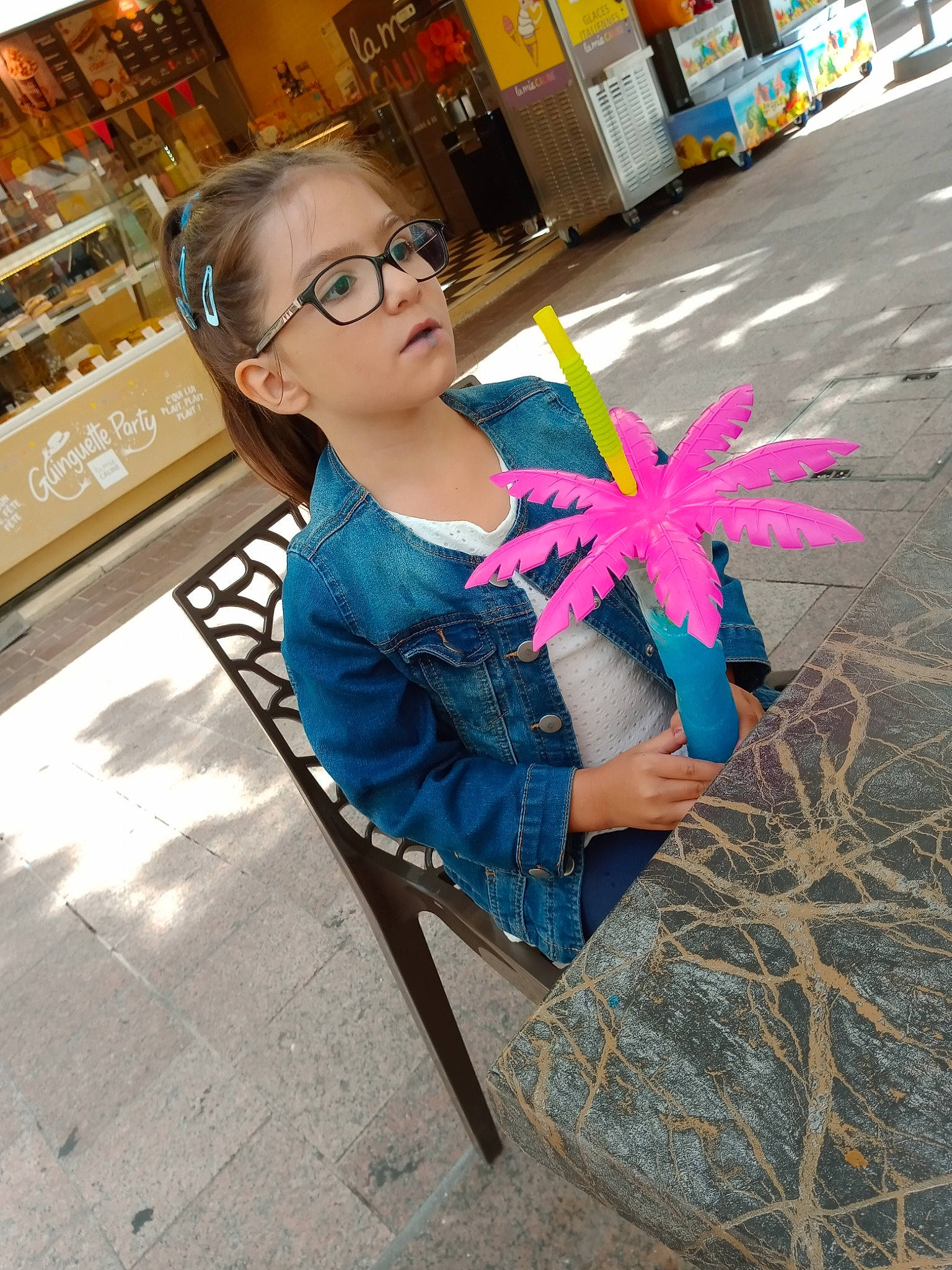 Inaya participe au concours pour gagner de l'argent avec cette photo : art, automotive_wheel_system, electric_blue, eyewear, fashion_accessory, fun, glasses, human_settlement, leisure, magenta, party_supply, person, road_surface, sidewalk, sitting, street, toddler, toy, tree, vision_care