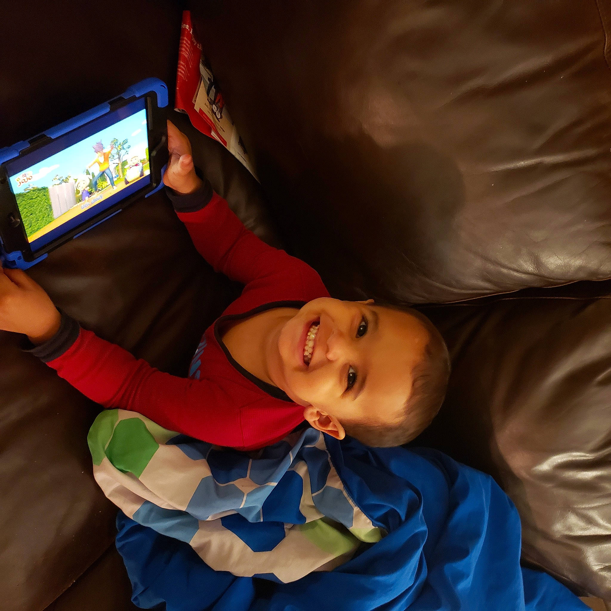 Enoch is registered to the contest to win money with this photo: child, comfort, communication_device, display_device, elbow, fun, gadget, happy, joy, leisure, linens, mobile_device, person, play, recreation, room, sleep, smile, tablet_computer, toddler
