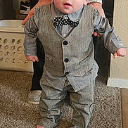 Skyler is registered to the contest to win money with this photo: toddler, child, vest, bow_tie, carpet, barefoot, tattoo, adult_hands, plaid_shirt, pants, indoor, laundry_basket, person, standing, supporting_hands, home, cute, young_child, carpeted_floor, casual