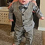 toddler, child, vest, bow_tie, carpet, barefoot, tattoo, adult_hands, plaid_shirt, pants, indoor, laundry_basket, person, standing, supporting_hands, home, cute, young_child, carpeted_floor, casual