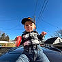 Skyler joined the competition — help win amazing prizes! toddler, child, boy, cap, hat, jeans, shirt, plaid_shirt, toy, car, outdoor, daylight, blue_sky, trees, house, residential_area, person, facial_expression, holding, clothing