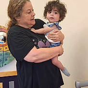 Athena is registered to the contest to win money with this photo: black_shirt, camouflage_pants, child, comfort, curly_hair, expression, floor, hand, heater, holding, indoor, interaction, love, mirror, person, playroom, sock, toddler, wall, woman