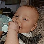 Christopher is registered to the contest to win money with this photo: baby, infant, bottle, smiling, blue_eyes, face, chubby_cheek, hand, arm, safety_strap, baby_seat, onesie, feeding, close_up, portrait, indoors, cushion, fabric, happy, home