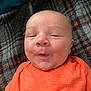 Gary joined the competition — help win amazing prizes! baby, infant, orange_shirt, plaid_blanket, face, expression, puckered_lips, lying_down, cute, skin, head, child, person, indoors, sleepy, closeup, cozy, soft_texture, young, portrait