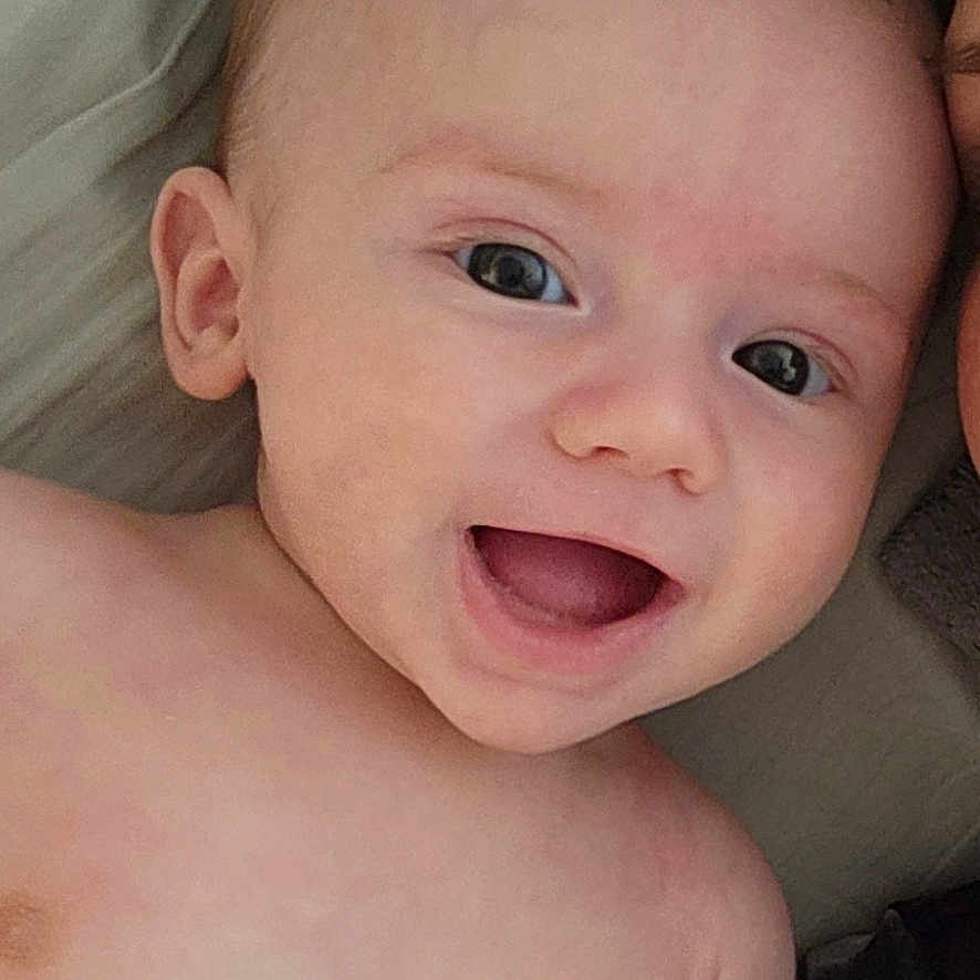 Ryker is registered to the contest to win money with this photo: baby, bed, bedroom, bodypart, cushion, face, furniture, happy, head, homedecor, indoors, laughing, mouth, newborn, person, photography, portrait, room, smile, teeth