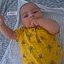 baby, blanket, blue_pants, child, cute, face, gray_blanket, hand_in_mouth, indoors, infant, lying_down, palm_tree_pattern, person, short_sleeves, skin, soft_texture, striped_blanket, toddler, yellow_shirt, young_child