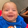 apparel, baby, blue_shirt, casual_wear, child, citrus_design, close_up, cute, face, happy, indoor, infant, person, portrait, seated, skin, smiling, stroller, tiled_floor, young_child