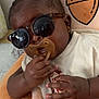 baby, sunglasses, pacifier, hand, pillow, acorn, earring, clothing, infant, cute, portrait, indoor, child, relaxing, soft_toy, accessory, person, face, skin, young