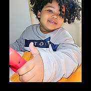 Kamaiyha joined the competition — help win amazing prizes! child, smiling, curly_hair, thumbs_up, blanket, indoor, portrait, happy, person, clothing, hair_accessory, cute, young, casual, face, hand, red_object, cozy, positive_gesture, home