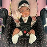 baby, infant, child, car_seat, harness, pacifier, headband, floral_clothing, pink, plush_toy, sitting, portrait, wide_eyes, indoors, vehicle, safety, blanket, cushion, baby_clothing, photography