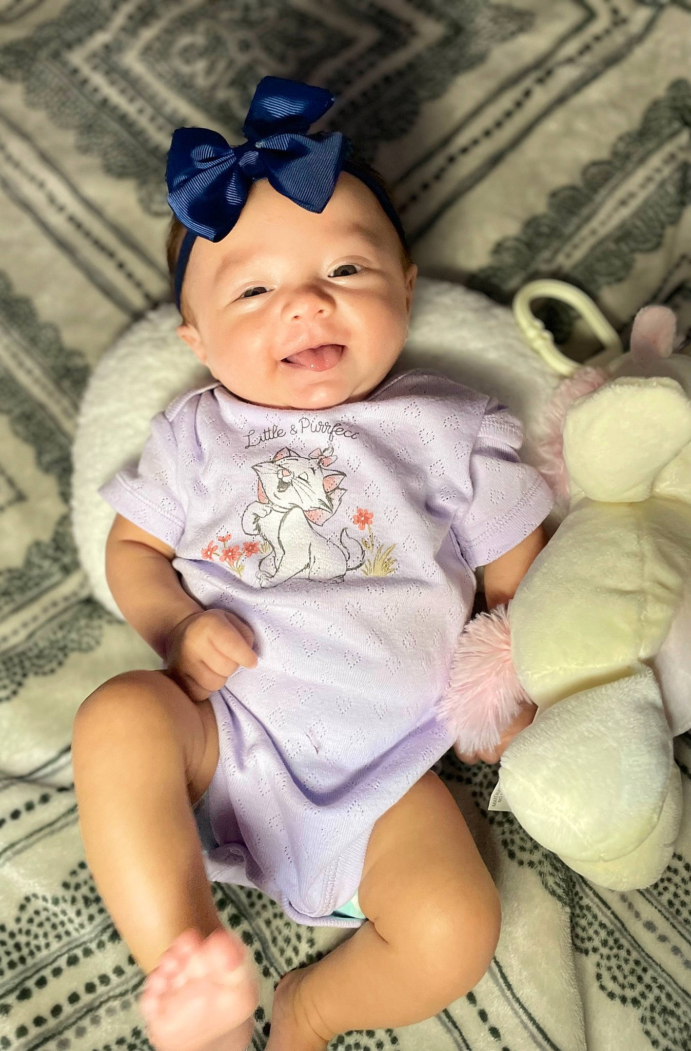 Athena is registered to the contest to win money with this photo: baby, baby_products, baby_toddler_clothing, beanie, cap, cheek, child, eye, fashion_accessory, foot, happy, headwear, human_leg, pattern, person, pink, purple, sitting, skin, smile