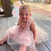 Hazely joined the competition — help win amazing prizes! baby, child, girl, pink_dress, headband, smile, sitting, wooden_floor, outdoor, patio, chairs, tables, sunlight, necklace, happy, cute, tulle, ribbons, person, portrait
