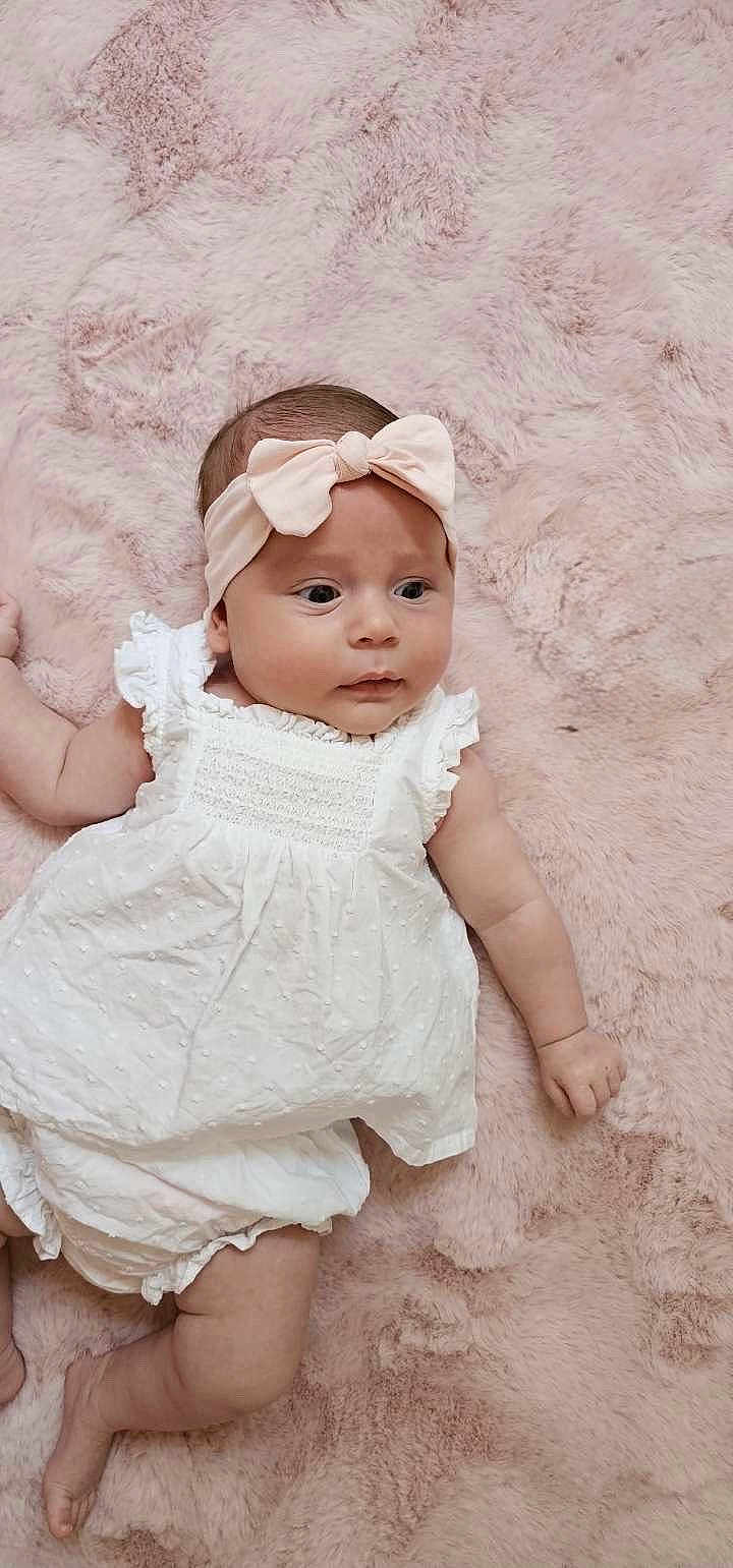 Mileena a rejoint le concours — aidez-le/la à gagner de superbes lots ! baby, infant, child, headband, bow, white_dress, soft_blanket, pink_background, skin, face, eyes, arm, leg, cute, newborn, lying_down, indoors, portrait, adorable, chubby