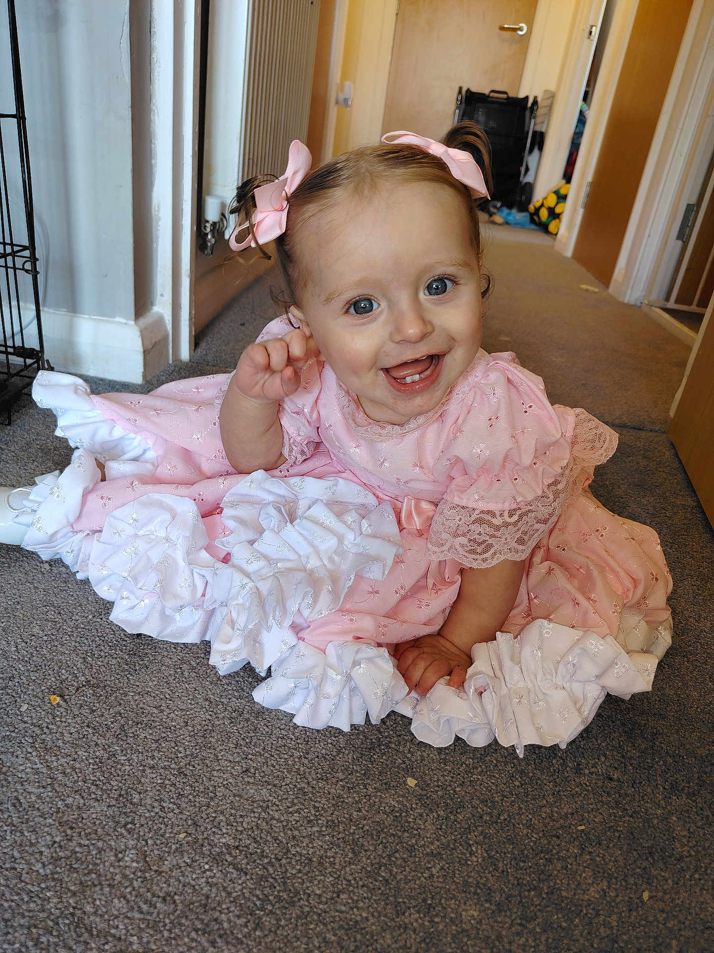 Lila-Rose is registered to the contest to win money with this photo: baby, child, girl, pink_dress, ruffles, smiling, happy, carpet, indoor, home, hair_bows, pigtails, person, cute, infant, floor, hand_raised, blue_eyes, portrait, candid