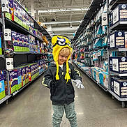 Robert joined the competition — help win amazing prizes! balloons, boxes, child, concrete_floor, gloves, hoodie, indoor, kid, minion_hat, pants, party_supplies, person, playful, retail, shelves, shopping, smiling, sneakers, store_aisle, yellow_hat