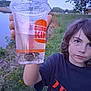 Bryce is registered to the contest to win money with this photo: child, boy, cup, burger_king, crab, water, riverbank, grass, outdoor, nature, hand, face, tshirt, blue_eyes, evening, toy, animal, person, portrait, holding