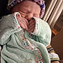 newborn, baby, sleeping, blanket, knit_hat, hand, person, adult_hand, wristband, cozy, indoor, soft, cute, infant, closeup, wearing, pattern, floral, peaceful, resting