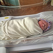 Emiley is registered to the contest to win money with this photo: newborn, baby, blanket, hospital, bassinet, sleeping, hat, wrapped, infant, crib, bed, person, indoor, wooden_door, floor, hospital_room, resting, peaceful, soft, child