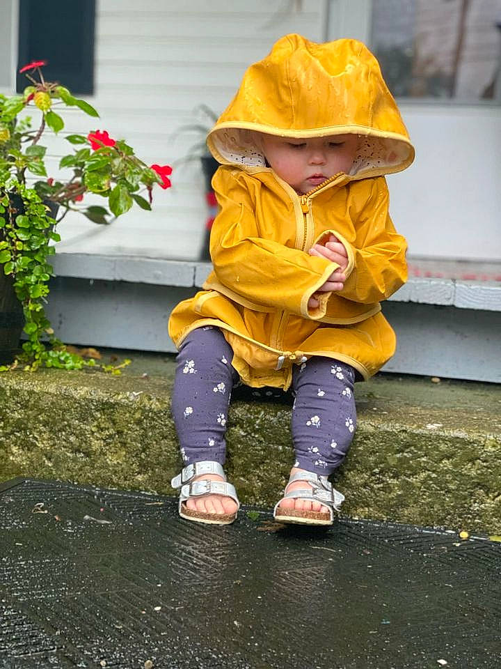 Elodie is registered to the contest to win money with this photo: boot, cap, child, flower, foot, grass, hat, headwear, human_leg, jacket, lawn_ornament, person, plant, play, road_surface, shoe, sitting, sleeve, sneakers, sunglasses