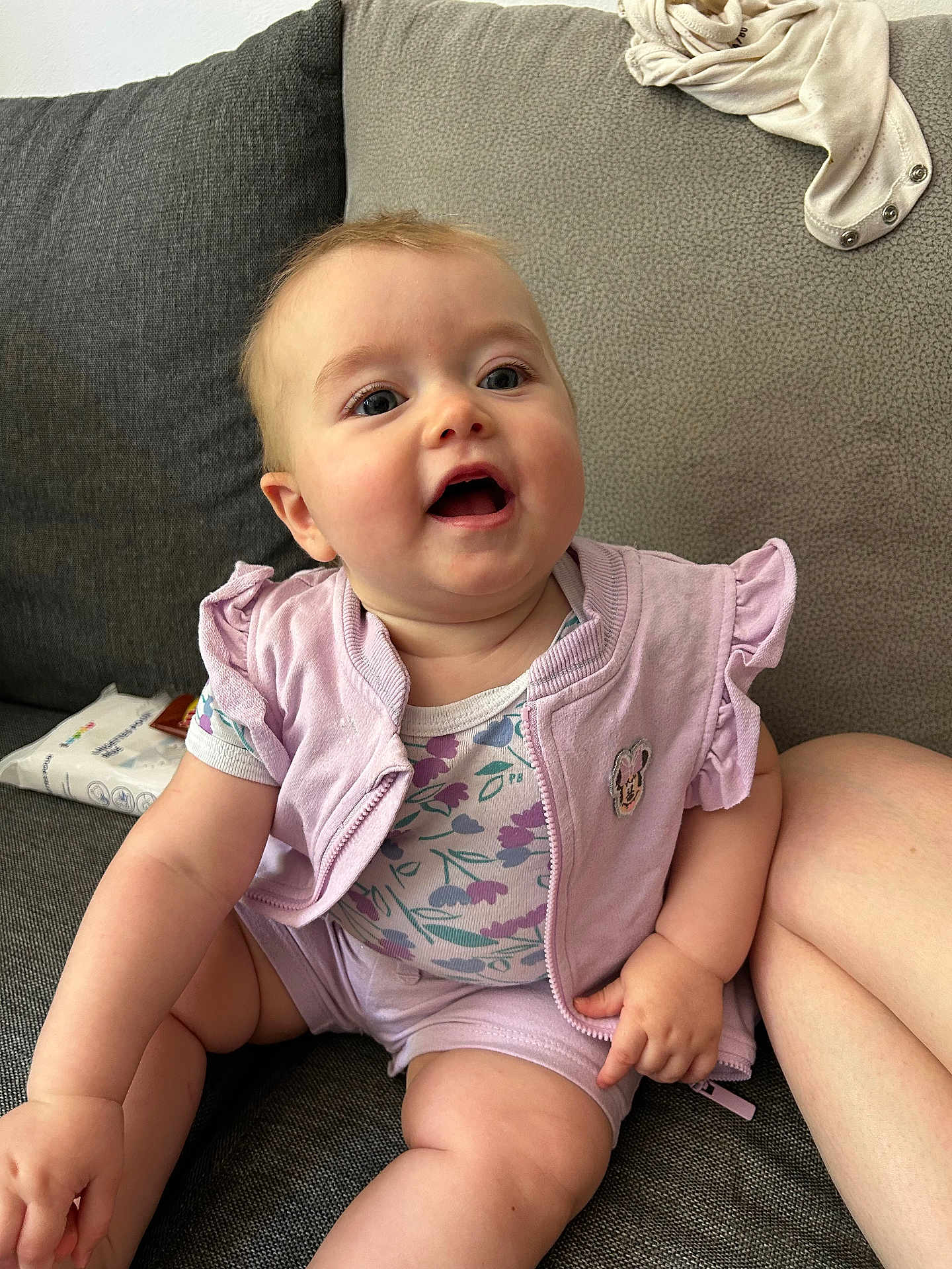 Maëly a rejoint le concours — aidez-le/la à gagner de superbes lots ! baby, child, infant, sitting, couch, clothing, vest, onesie, floral_pattern, happy, smiling, skin, face, arm, leg, indoor, furniture, soft_toys, cute, young