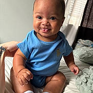 Syaire is registered to the contest to win money with this photo: baby, child, blue_onesie, dinosaur_emblem, tongue_out, smiling, sitting, bed, blanket, white_socks, tattooed_hand, natural_light, curtains, indoor, cute, portrait, skin, infant, happy, person