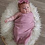 baby, infant, pink_bow, blanket, fluffy_rug, basket, wooden_floor, headband, cute, chubby_cheeks, wrapped, lying_down, indoors, soft_texture, portrait, closeup, child, adorable, peaceful, small_hand