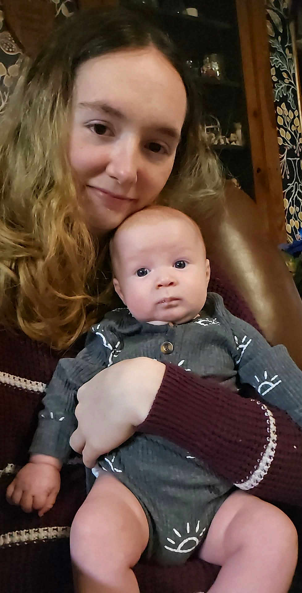 Eric joined the competition — help win amazing prizes! baby, infant, child, woman, face, hands, holding, arm, sweater, onesie, seated, couch, living_room, hair, eyes, portrait, looking_at_camera, furniture, curtains, cabinet