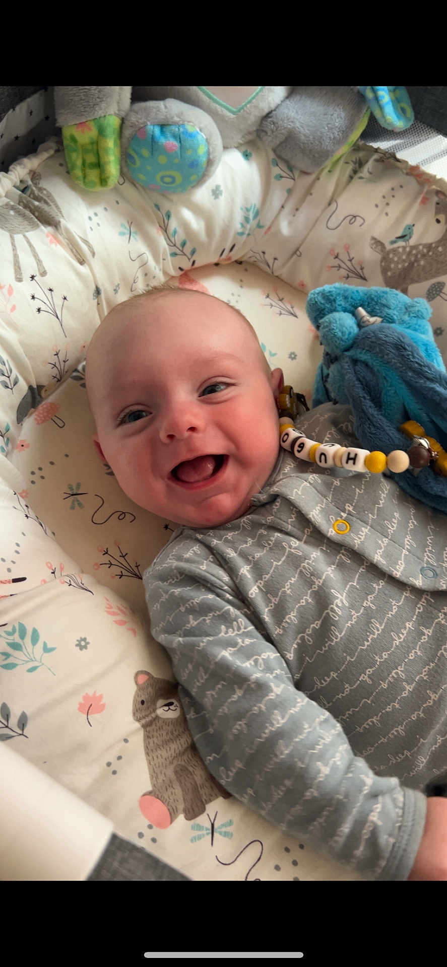 Hugo a rejoint le concours — aidez-le/la à gagner de superbes lots ! baby, smiling, infant, toy, cushion, patterned_fabric, blue, grey_clothing, cute, lying_down, happy, face, child, soft_toy, indoors, comfort, young_child, person, expression, closeup