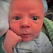 Ledger is registered to the contest to win money with this photo: baby, newborn, infant, face, expression, hand, fist, blanket, onesie, close_up, skin, cute, indoors, portrait, young, child, sleepwear, resting, cozy, curious