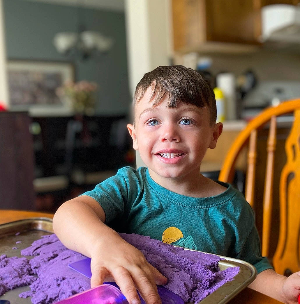 Kayden is registered to the contest to win money with this photo: baby_toddler_clothing, baking, chair, child, comfort_food, dessert, facial_expression, fun, hairstyle, happy, joy, leisure, person, picture_frame, play, purple, sharing, sitting, sleeve, smile