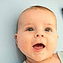 baby, close_up, face, happy, infant, mouth_open, blue_background, child, cute, eyes, expression, patterned_cushion, portrait, skin, head, smile, young, baby_clothing, indoors, cheerful