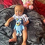 baby, child, blanket, plush_toy, stuffed_animal, hello_kitty, bed, pillow, comfort, indoor, cute, smiling, toddler, soft_texture, relaxing, cartoon_character, foot, hand, clothing, portrait