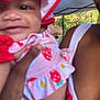 baby, child, smiling, hat, strawberry_pattern, pink_clothing, adult_hand, outdoor, canopy_tent, trees, shoulder, arm, person, face, close_up, summer, daylight, nature, holding, cute