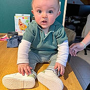Mahëlo participe au concours pour gagner de l'argent avec cette photo : baby, child, table, green_sweater, striped_pants, white_shoes, indoor, person, wide_eyes, curious, hand, wood, floor, box, background, clothing, sitting, expression, face, home