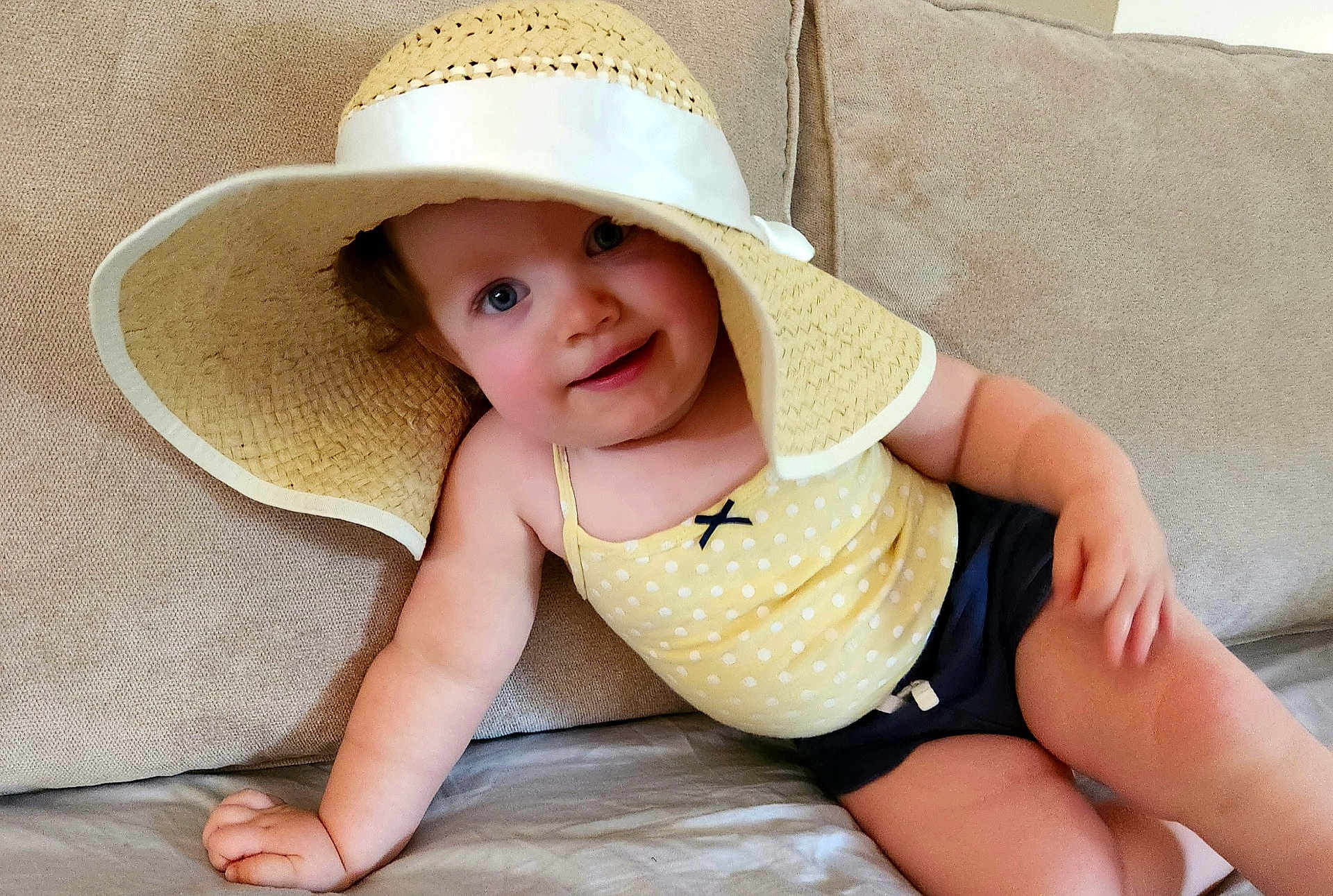 Kloe joined the competition — help win amazing prizes! baby, child, hat, yellow_top, polka_dot, couch, beige, smile, blue_eyes, shorts, infant, indoors, skin, arm, hand, face, headwear, relaxed, portrait, cute
