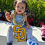 Deonni joined the competition — help win amazing prizes! toddler, child, curly_hair, gold_chain, giant_pendant, blue_dress, white_tights, sneakers, outdoor, sunlight, greenery, flowers, red_flowers, snack, sitting, cute, portrait, fashion, accessories, playful