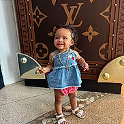 Deonni is registered to the contest to win money with this photo: toddler, child, smile, standing, clothing, dress, sandals, necklace, curly_hair, floor, pattern, luxury_brand, background, indoor, portrait, person, happy, fashion, accessory, cute