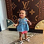toddler, child, smile, standing, clothing, dress, sandals, necklace, curly_hair, floor, pattern, luxury_brand, background, indoor, portrait, person, happy, fashion, accessory, cute