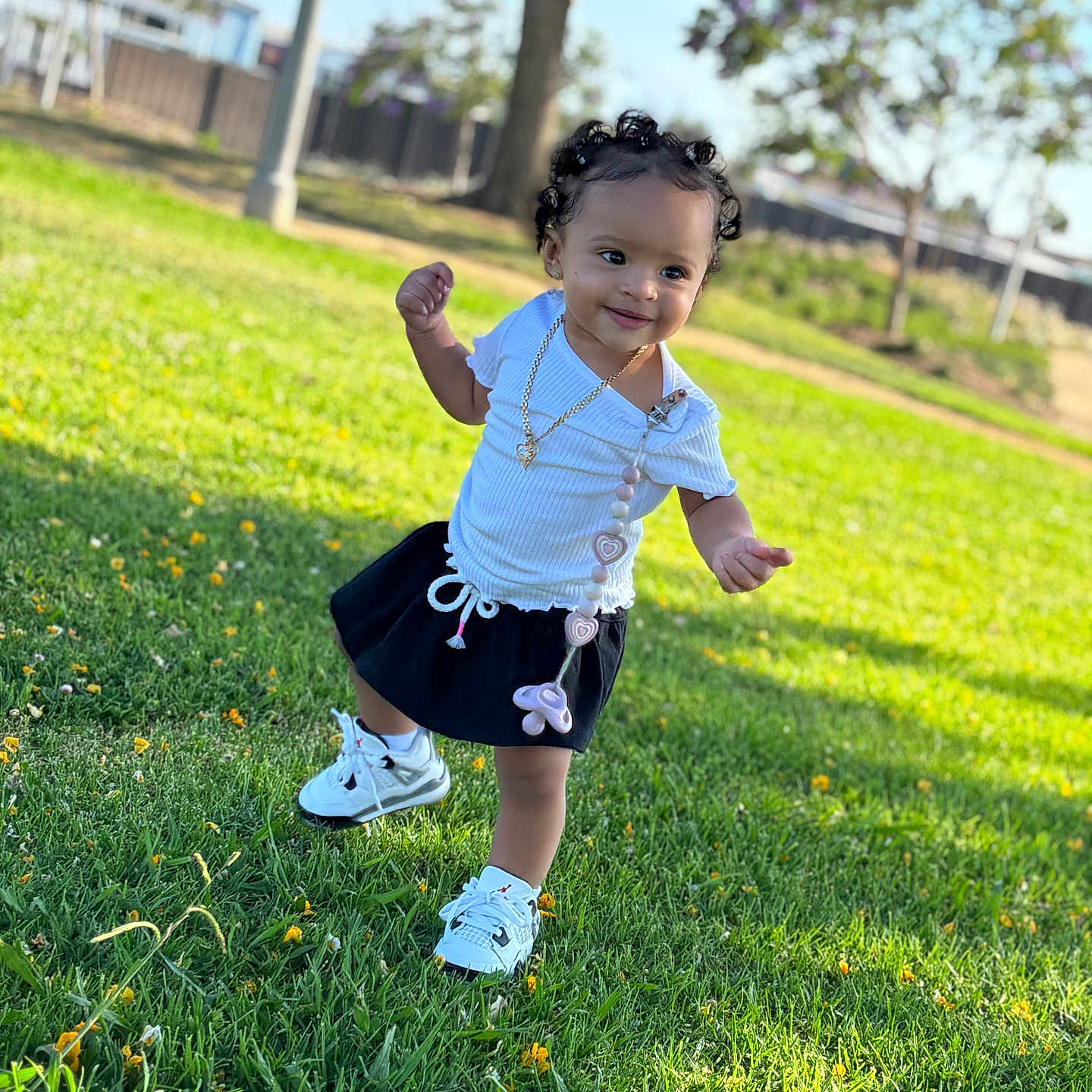Deonni is registered to the contest to win money with this photo: blue_sky, child, curly_hair, cute, daylight, fence, grass, happy, nature, outdoor, pacifier_clip, park, skirt, smiling, sneakers, sunny, toddler, tree, walking, white_shirt